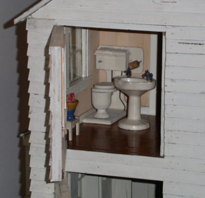 [Room has a dark wooden floor, a pedastal sink, a toilet with a tank on the wall above the bowl, and a small stool. A window is in the wall beside the toilet.]